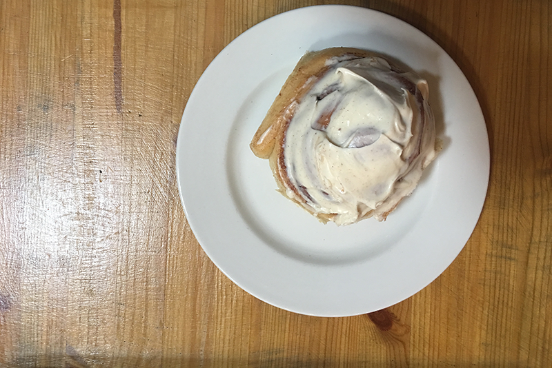 Cinnamon bun with white icing on a wooden table